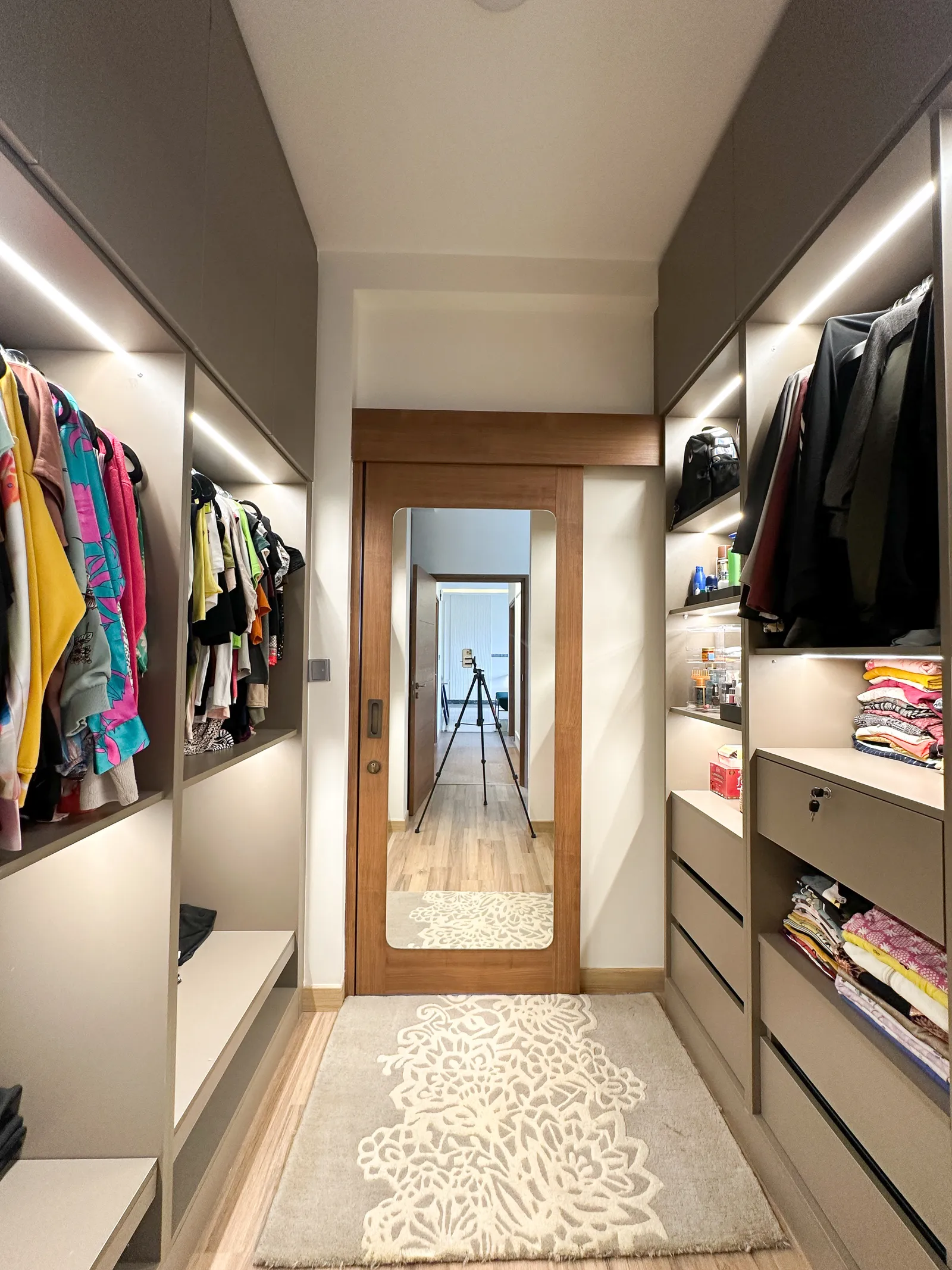 Walk-in wardrobe with lit hanging and shelf units on both sides — Somani's Residence